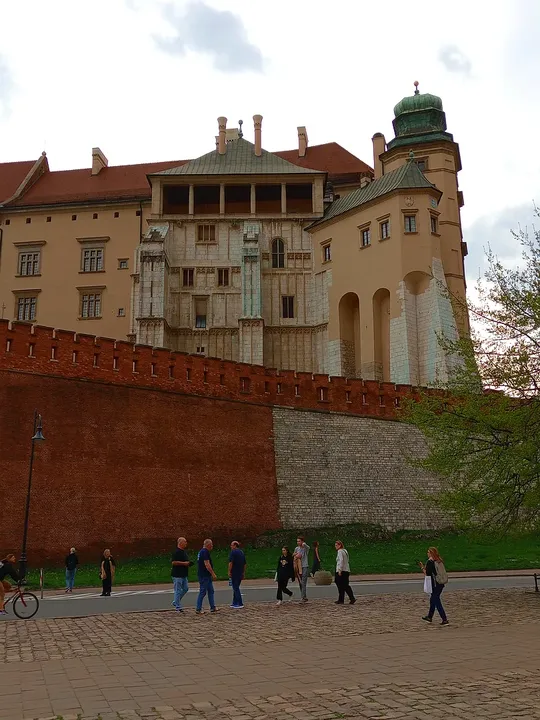 People walking beneath the castle wall at Father Adam Studziński Square