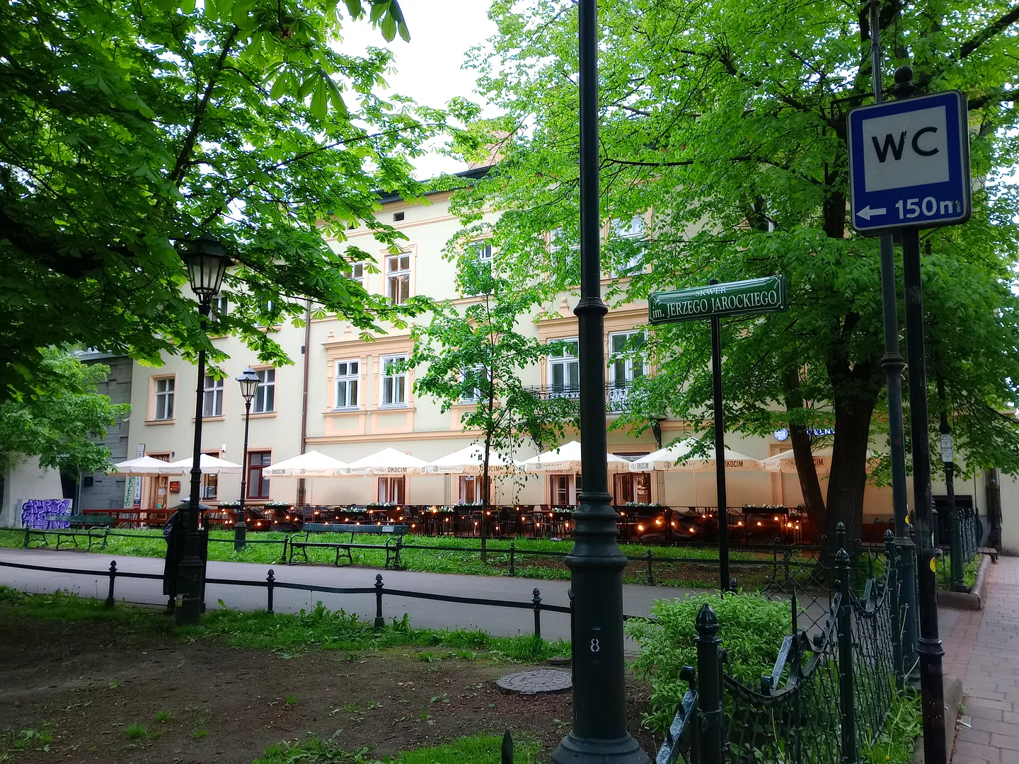 A bench and railings beneath spring trees at Jerzy Jarocki Square