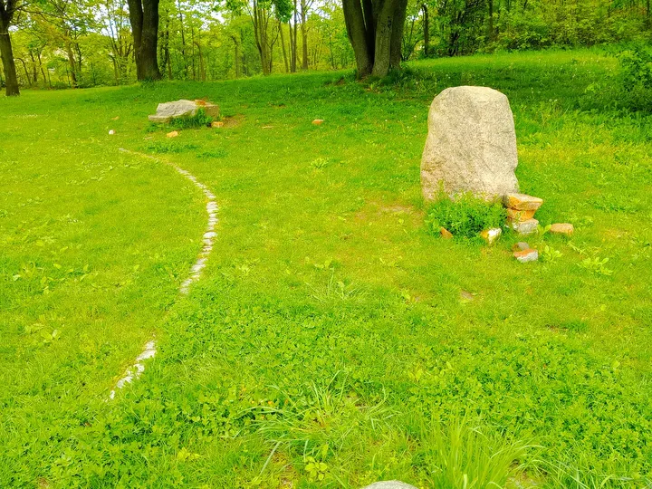 Stone marker beside a curved line of pale stones at Peace Bells Garden, Kraków
