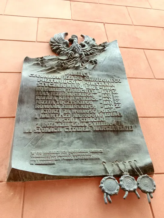 Commemorative panel on the salmon-coloured wall at Pijarska Street