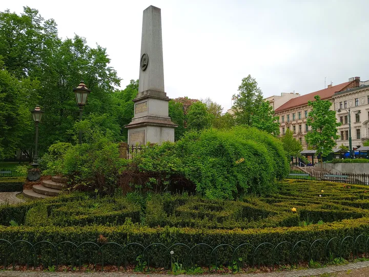 A monument beyond clipped planting at Planty: Station Garden