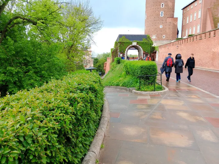 Visitors walk along the path beside the castle walls and spring greenery on Wawel Hill in Kraków