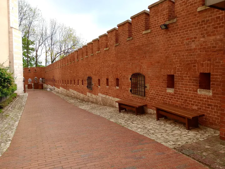 A paved path follows the red-brick defensive walls on Wawel Hill in Kraków