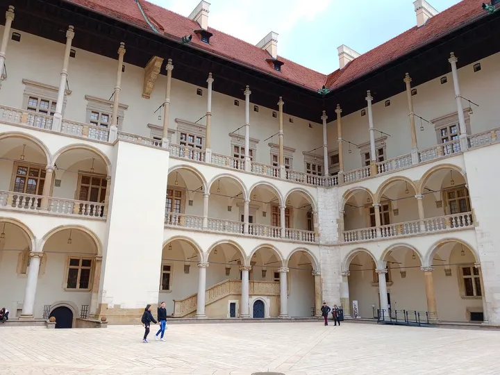 The arcades continue around a corner, with people below giving a sense of the courtyard’s scale on Wawel Hill in Kraków