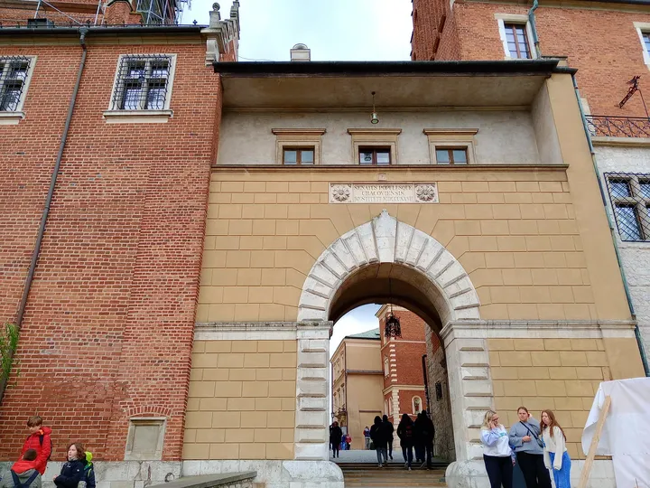 Visitors pass through a stone-framed entrance beneath the hill’s buildings on Wawel Hill in Kraków