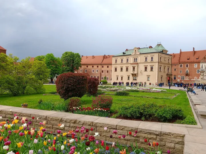 Flower beds and clipped hedges sit between the path and the castle buildings on Wawel Hill in Kraków