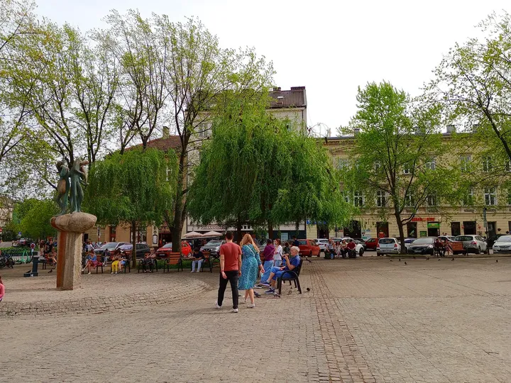 People walking beneath the square’s trees at Wolnica Square