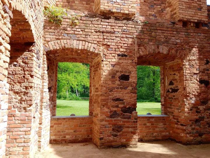 Arched window openings in exposed brick walls with the green park beyond, in Zatonie Ducal Park